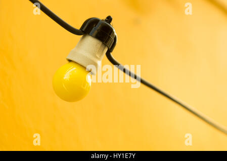 Yellow bulb hanging on a yellow wall.