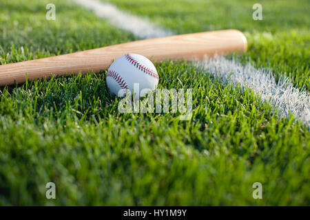 A selective focus view of a baseball bat and ball on the grass near a field stripe Stock Photo