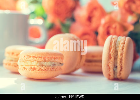 Orange mango or citrous macaroons and orange fresh little roses on light wooden background. Coloring and processing photo with light vintage style. To Stock Photo
