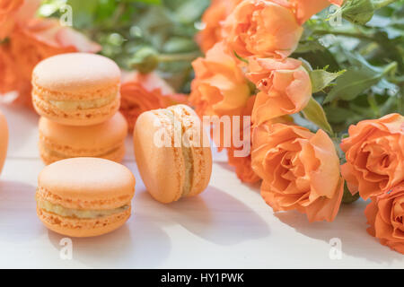 Orange mango or citrous macaroons and orange fresh little roses on light wooden background. Coloring and processing photo with light vintage style. To Stock Photo