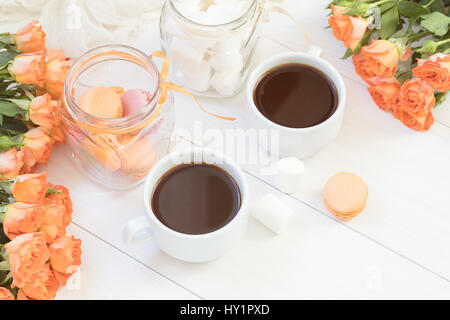 Orange mango macaroons, cup of coffee, marshmallow and fresh little roses on light wooden background. Sunlight. Coloring and processing photo with lig Stock Photo