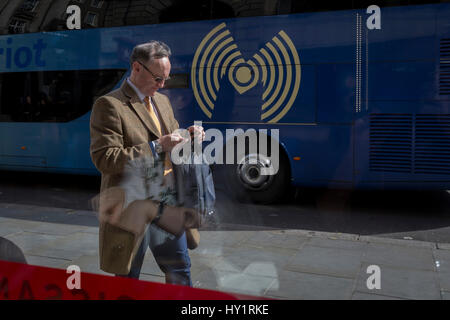 Man checks messages while passing Wifi symbol, on 30th March 2017, in London, England. Stock Photo