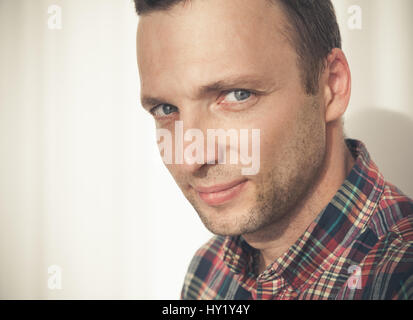 Close-up studio face portrait of young adult European man in colorful casual shirt over white wall with shadow Stock Photo