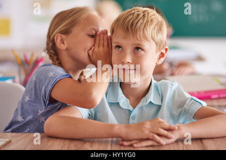 Boy and girl whispering in classroom Stock Photo