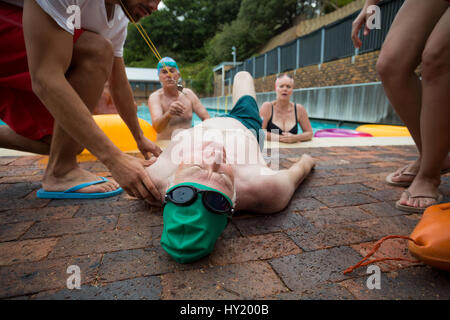 Worried lifeguards and friends looking at unconscious senior man at poolside Stock Photo