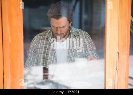 Young man using mobile phone in cafe seen through window Stock Photo
