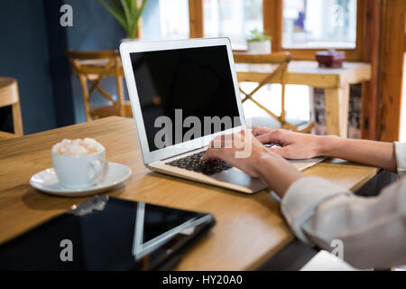 Cropped image of young woman using laptop at table in careteria Stock Photo