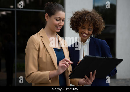 Two businesswomen using digital tablet near office building