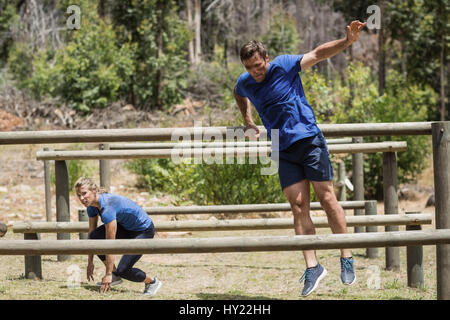 Man and woman jumping over the hurdles during obstacle course in boot camp Stock Photo