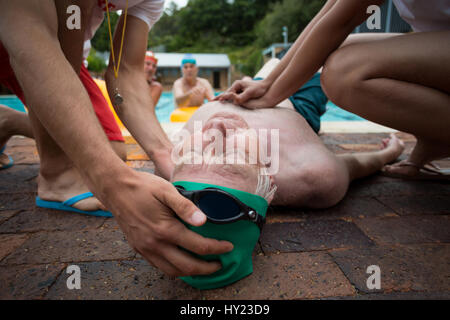Lifeguards pressing chest of unconscious senior man at poolside Stock Photo