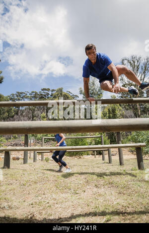 Man and woman jumping over the hurdles during obstacle course in boot camp Stock Photo