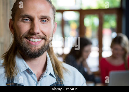 Portrait of confident male barista with female customers in background at coffee shop Stock Photo