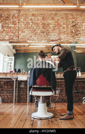 Male hairdresser trimming hair of customer at his shop. Hairstylist doing haircut using hair clipper at barber shop. Stock Photo