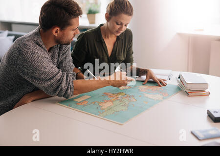 Man and woman discussing and making notes pointing at the world map. Young couple looking at the world map on a study table. Stock Photo