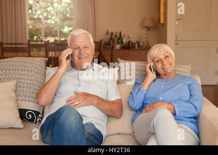 Happy seniors sitting at home talking on cellphones Stock Photo