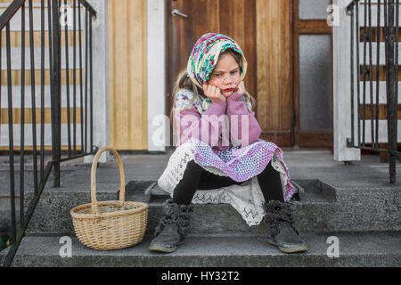 Sweden, Pensive girl (4-5) dressed up as Easter witch with Easter basket sitting on steps Stock Photo