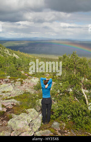 Sweden, Dalarna, Fulufjallet, Man standing on hill and looking at landscape with rainbow