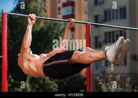 Young muscular build man doing pull ups exercises on horizontal bar outdoors. Stock Photo