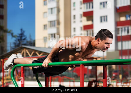 Fit man workout out arms on dips horizontal bars training triceps and biceps doing push ups outdoors. Stock Photo