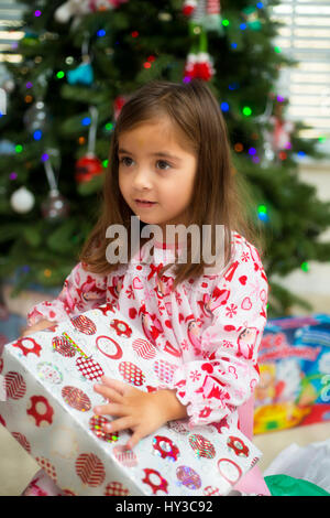 little girl opening  Christmas presents and tree behind her Stock Photo