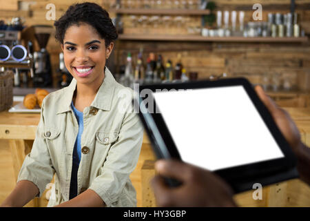 Portrait of smiling female customer with barista holding tablet PC in foreground at cafe Stock Photo