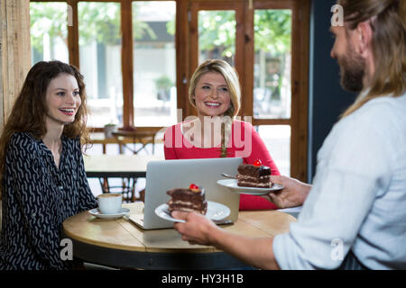 Male barista serving dessert to female customers in coffee shop Stock Photo
