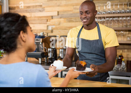 Portrait of male barista serving coffee and dessert to female customer in cafe Stock Photo