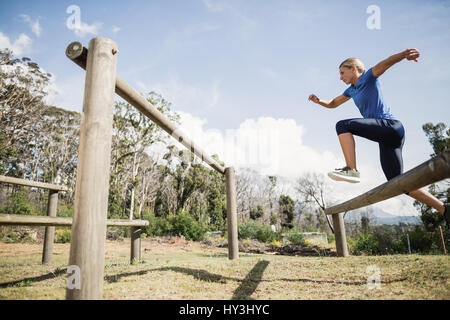 Woman jumping over the hurdles during obstacle course in boot camp Stock Photo