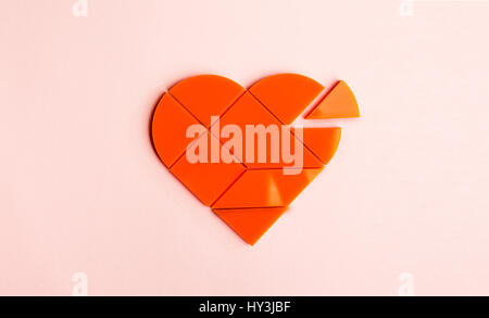 Plastic puzzle in the form of heart with disconnected piece on a pink background Stock Photo