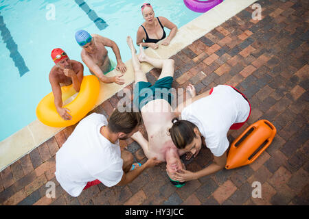 High angle view of friends looking at lifeguards saving unconscious senior man at poolside Stock Photo