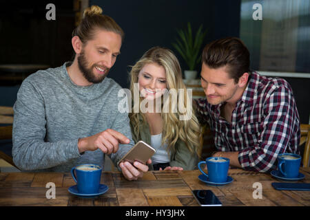 Young man showing smart phone to friends at table in coffee shop Stock Photo