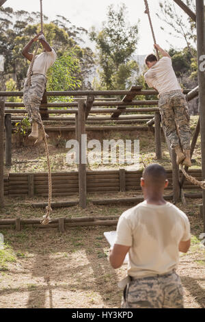 Military soldiers climbing rope during obstacle course training at boot camp Stock Photo