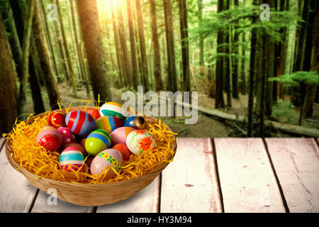 Multi colored easter eggs in wicker basket against tall trees growing in forest Stock Photo