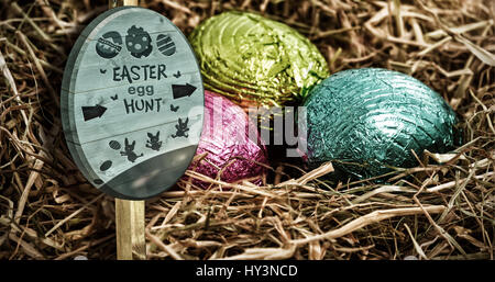 Easter egg hunt sign against three colouful easter eggs nestled in straw nest Stock Photo