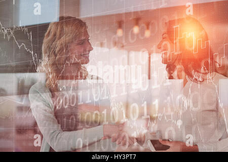 Stocks and shares against businesswomen shaking hands in office Stock Photo