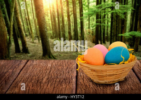 Colorful Easter eggs in wicker basket  against tall trees growing in forest Stock Photo