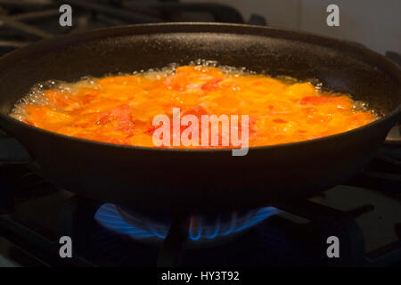 Red and yellow tomatoes cooking in cast iron frying pan over flame on gas stove. Stock Photo