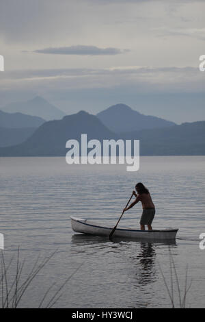 Local male person in Guatemala standing in his boat and swimming towards the other side of lake Stock Photo