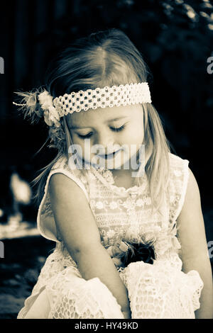 Little toddler girl sitting and looking down wearing an old fashioned dress Stock Photo