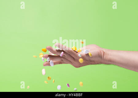 Colored pills falling from hand on green background. Stock Photo