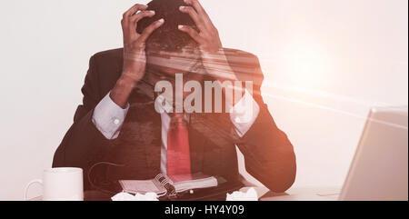 Light trails on city street against frustrated afro businessman with head in hands at desk Stock Photo