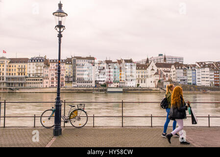 Two young women walking on Basel riverfront opposite Basel's Altstadt ('old town') on the footpath along the Rhine River. Stock Photo