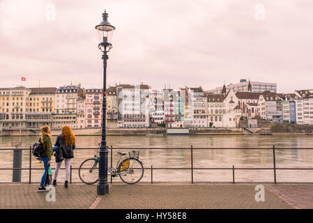 Two young women, bike and street lamp on Basel riverfront opposite Basel's Altstadt ('old town') on the footpath along the Rhine River. Stock Photo