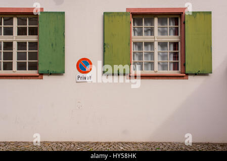 Wooden old medieval windows with green shutters on empty white wall with no parking sign and Privat (Private) written below Stock Photo