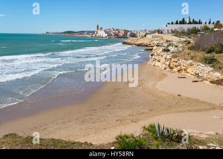 Beach and rocky coast with view of the beautiful town of Sitges, Spain in the background. Stock Photo