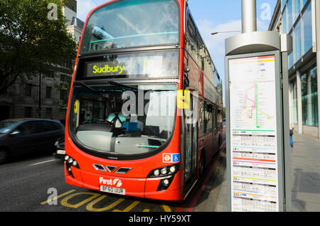 A red double-decker London bus passes a bus stop showing a stylised map and timetables. Bus frequencies; public transport in Britain, British bus Stock Photo