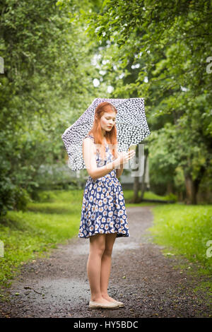 Finland, Pirkanmaa, Tampere, Woman wearing floral dress standing with umbrella in park