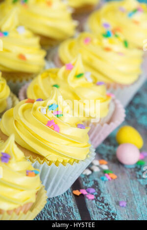 Row of yellow Easter cupcakes with candy and sprinkles on vintage wooden table Stock Photo