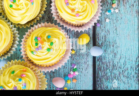 Yellow Easter cupcakes with candy and sprinkles on vintage wooden table. Top view. Stock Photo