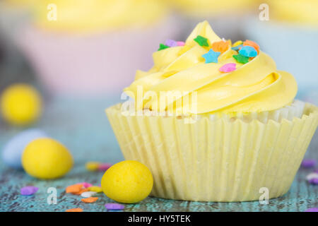 Yellow Easter cupcake with candy and sprinkles on vintage wooden table. Closeup with shallow depth of field. Stock Photo